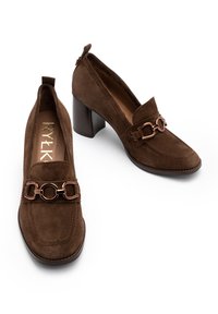 Brown suede loafers featuring a chunky heel, decorative metal chain accent, and stitching detail along the upper edge. Classic design.
