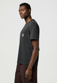 Zwarte katoenen t-shirt met een ronde hals, korte mouwen en een zak met een klein logo. De pasvorm is ontspannen en casual.