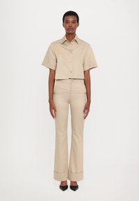 Beige cropped shirt with a button-up front and short sleeves, paired with high-waisted, flared pants. Black pointed-toe shoes.