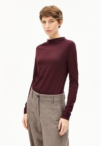 Bordeaux top met lange mouwen en hoge kraag, in combinatie met beige textuurbroek. Soepele stof met een aansluitende silhouet.