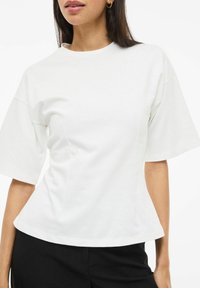 Biała koszulka z krótkim rękawem o okrągłym dekolcie, dopasowanym kroju i gładkiej bawełnianej fakturze, zestawiona z czarnymi spodniami.