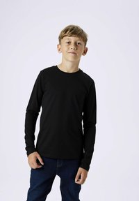 Langarm schwarzes Baumwoll-T-Shirt mit Rundhalsausschnitt. Glatte Textur, körperbetontes Design, kombiniert mit blauen Jeans.