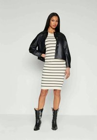 Juoda odinė trumpa striukė dėvima ant baltos ir juodos dryžuotos prigludusios suknelės. Juodi kelio ilgio batai su baltomis gėlėmis.