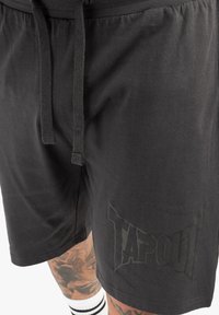 Schwarze Baumwollshorts mit einem Kordelzug, ausgestattet mit einem strukturierten "TAPOUT"-Logo auf der linken Seite. Glatte Oberfläche und lockere Passform.