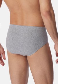 Brief grigi in cotone con vestibilità a vita media, caratterizzati da una superficie liscia e una cintura elastica, mostrati da dietro in un ambiente neutro.
