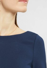 Granatowa bluzka z szerokim dekoltem, gładką fakturą i krótkimi rękawami. Posiada minimalne detale przeszycia wzdłuż szwów na ramionach.