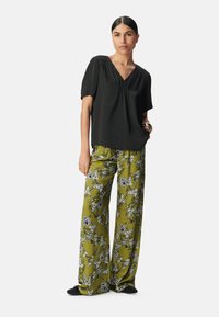 Schwarze kurzärmlige Bluse mit V-Ausschnitt und Raffung, kombiniert mit hochgeschnittenen, weit geschnittenen Hosen in olivgrünem Blumenmuster. Glatte Textur.