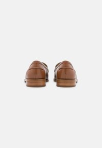Bruine leren schoenen gezien vanaf de achterkant met lage houten hakken op een witte achtergrond.
