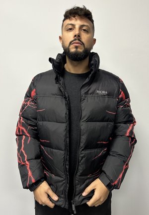 Giacca a vento nera con grafiche di fulmini rossi, chiusura con zip, collo alto e polsini elasticizzati. Il materiale appare lucido e texture.