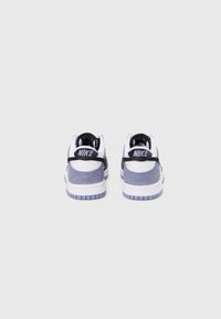 Nike-tennarit, joissa on valkoinen nahkapäällinen, harmaat mokkakoristeet, musta kantatuki ja sininen kumipohja. Takana tunnusomainen logo.