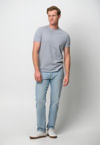 Grå kortärmad t-shirt, ljusblå jeans och vita sneakers med bruna sulor. Avslappnad passform och mjukt bomullsmaterial. Enkelt mönster.