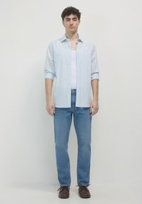 Chemise à rayures bleu clair et blanche avec un jean bleu et des chaussures marron foncé. Coupe décontractée avec un col classique et des manches longues.
