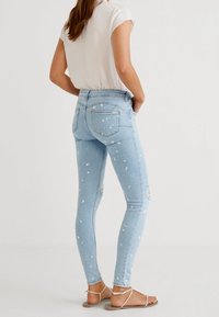 Jeans ajustados de color azul claro con detalles desgastados y salpicaduras de pintura blanca, que cuentan con un diseño clásico de cinco bolsillos y una cinturilla de altura media.