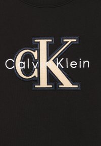Maglione nero con logo Calvin Klein ricamato; scritte color crema e blu navy con design audace della "K", tessuto morbido al tatto.
