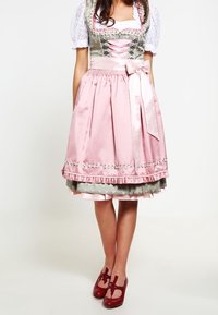 Pink and gray dirndl dress with a fitted bodice, lace-up front, puffed sleeves, and ruffled hem. Paired with red, rounded shoes.