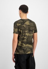 Camo t-shirt σε ελαιόλαδο χρώμα με πιο σκούρους πράσινους και μαύρους σχεδιασμούς, κοντά μανίκια, στρογγυλή λαιμόκοψη και μαλακό βαμβακερό υλικό.