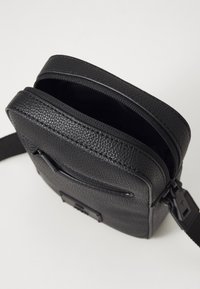 Borsa a tracolla in pelle nera con superficie texturizzata, chiusura superiore con zip, tracolla regolabile e tasca anteriore a scomparsa.