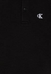 Zwarte polo met een gestructureerde stof, voorzien van een drie-knopen sluiting en een geborduurd wit "cK" logo op de linkerborst.