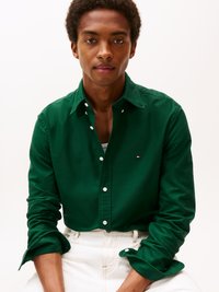 Grüne Hemdjacke aus Baumwolle, mit Kragen, langen Ärmeln und einem kleinen Logo-Detail. Kombiniert mit hellbeigen Hosen.