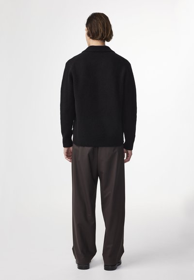 Maglione nero a maglia con colletto, taglio rilassato, maniche lunghe e orlo a costine. Abbinato a pantaloni marroni a gamba larga e scarpe nere.