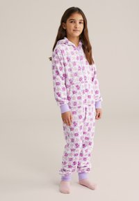 Fehér polár egyberuha lila virágmintákkal, kapucnival, elöl cipzárral és bordázott mandzsettákkal. Kényelmes viseletre alkalmas.