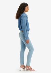 Denimskjorta i ljusblått med lång ärm och bröstficka. Slimmade ljusblå jeans kombinerade med vita klacksandaler. Ren, strömlinjeformad look.