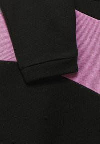 Svart klädessektion med ett rosa mönsterdetalj, med en slät textur och en ren skärning vid ärmen.