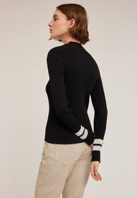 Schwarzer gerippter Langarmpullover mit weißen gestreiften Akzenten an den Bündchen. Figurbetonte Silhouette mit Rundhalsausschnitt und strukturiertem Stoff.
