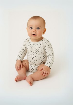 Bodysuit za bebe dugih rukava u krem boji s tamnim točkicama, s okruglim izrezom i mekanim materijalom. Beba sjedi s golim nogama, ruke su joj opuštene.
