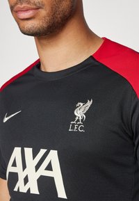 Svart sportströja med röda detaljer, försedda med en Nike-logotyp, silver Liverpool FC-emblem och vit text "AXA" på framsidan.