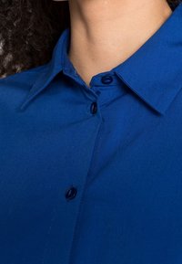 Blaues Hemd mit Knopfleiste und Kragen, mit glatter Textur, sichtbaren Knopfverschlüssen und ordentlich genähten Nähten.