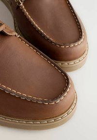 Brązowe skórzane buty z okrągłym noskiem, widocznymi przeszyciami i teksturowanym wykończeniem. Gumowa podeszwa z kontrastującym jasnobrązowym brzegiem.