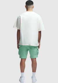 Weißes oversized T-Shirt mit kurzen Ärmeln, kombiniert mit mintgrünen Cargo-Shorts. Schuhdetails: Weiße Sneakers mit Knöchelsocken.