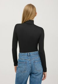 Czarny bodysuit z długim rękawem i stójką, zestawiony z niebieskimi dżinsami z wysokim stanem, które mają wyblakły kolor i dwie tylne kieszenie.