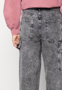 Pantalones cargo de mezclilla gris con una textura desgastada, que presentan múltiples bolsillos traseros y costuras en contraste; combinados con un sudadero rosa.