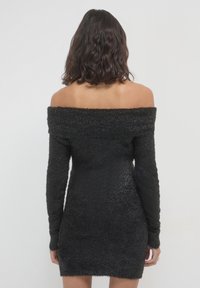 Schwarzes schulterfreies Kleid mit langen Ärmeln, aus einem samtigen, strukturierten Stoff, taillierte Silhouette und kurzer Länge. Einfaches Design ohne Muster.