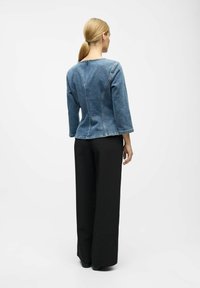 Jeansowa kurtka w ciemnoniebieskim kolorze, z rękawami 3/4 i dopasowanym krojem. Noszona z czarnymi spodniami o szerokich nogawkach i gładką teksturą.