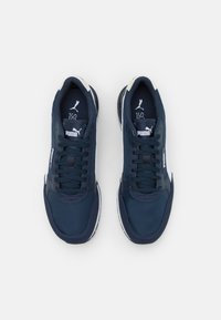 Des baskets de sport bleu marine avec une tige lisse, des accents blancs, un bout rond et une semelle noire épaisse ; logo présent sur la languette et sur le côté.