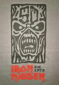 Šedé tričko s velkým černým grafickým motivem lebkové tváře s otevřenou pusou, po stranách doplněným oranžovým textem "IRON MAIDEN" a "Est. 1975".