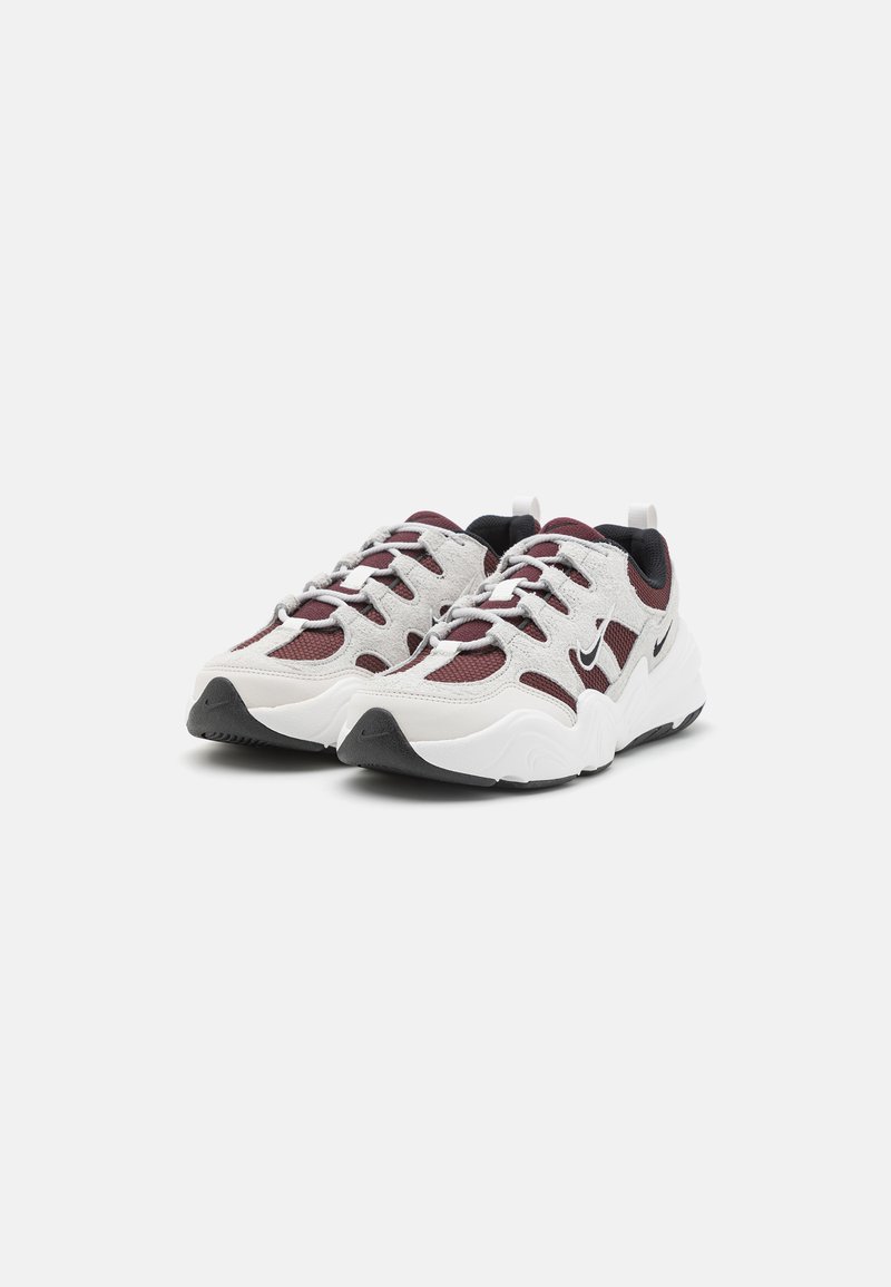 Sneaker bianche realizzate in mesh e suede, con accenti color maroon, suola in gomma nera e un sistema di allacciatura prominente.