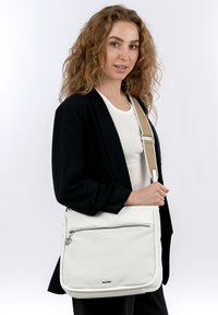 Borsa a spalla bianca in pelle con davanti testurizzato, scomparto con zip e tracolla regolabile. Design semplice, estetica moderna e hardware minimale.