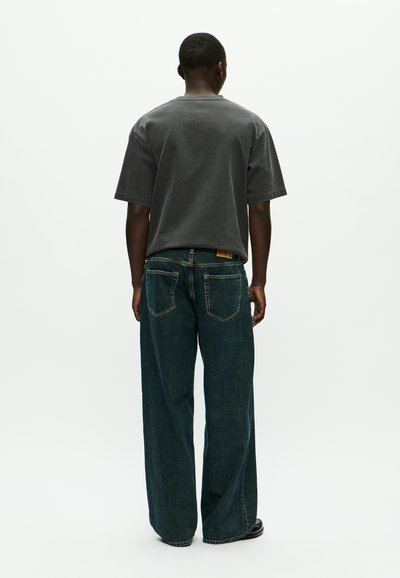 Grijze T-shirt met korte mouwen en wijd-uitlopende, donkerblauwe denim jeans. Opvallende details zijn een zichtbare tailleband-tab en lichte textuurvariaties.