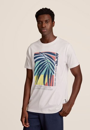 Witte katoenen t-shirt met een kleurrijke palmenbladgrafiek in blauwe, groene en rode tinten, en tekst aan de linkerkant.