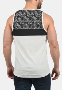 Herre ærmeløst tanktop med et sort og hvidt palmeblad mønster på ryggen, med en kremfarvet front og en sort accentstribe.