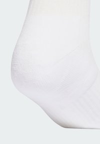 Hvid sok med et tekstureret strikkemønster, der har et glat tå- og hælområde. Stoffet virker blødt og fleksibelt.