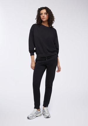 Felpa nera in cotone con scollo tondo e polsini a costine, abbinata a pantaloni jogger neri coordinati con vita elastica e coulisse.