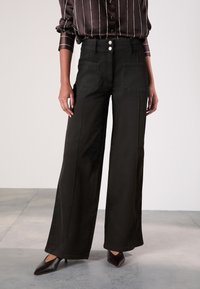 Sorte bukser med vide ben i tekstureret stof, med høj talje, to forlommer og dobbelte knapper som lukning.