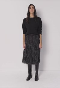 Suéter negro de punto combinado con una falda negra que presenta un patrón geométrico, de longitud hasta la rodilla con una capa transparente, y botas negras brillantes hasta la rodilla.