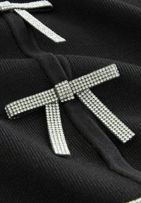 Czarna dzianina z dwoma dekoracyjnymi kokardkami wykonanymi z rhinestone'ów, o gładkiej fakturze i błyszczących akcentach podkreślających wzór.