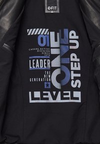 Zwarte jasvoering met blauw-witte grafische tekst: "01 ONE STEP UP LEADER THE NEW GENERATION LEVEL" met gelaagde texturen.